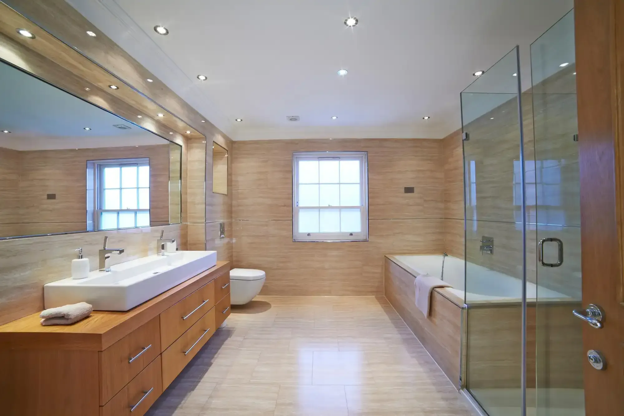 Spacious modern bathroom with double vanity, bathtub, glass shower, and beige tile walls