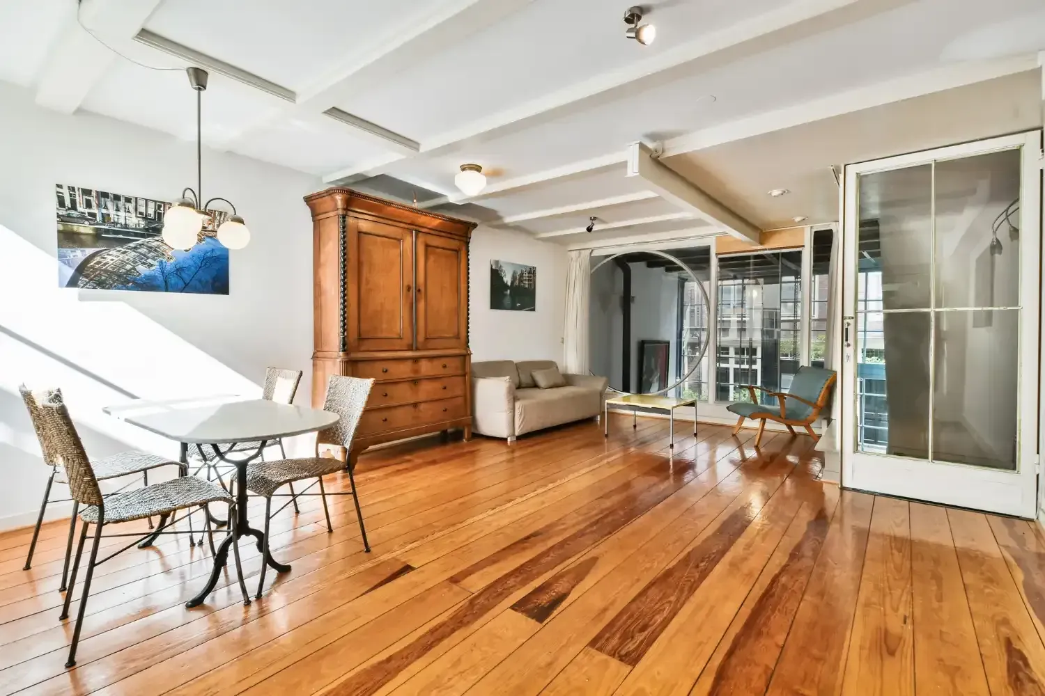 Living room with wood floors, large wooden cabinet, dining table, and access to a balcony.