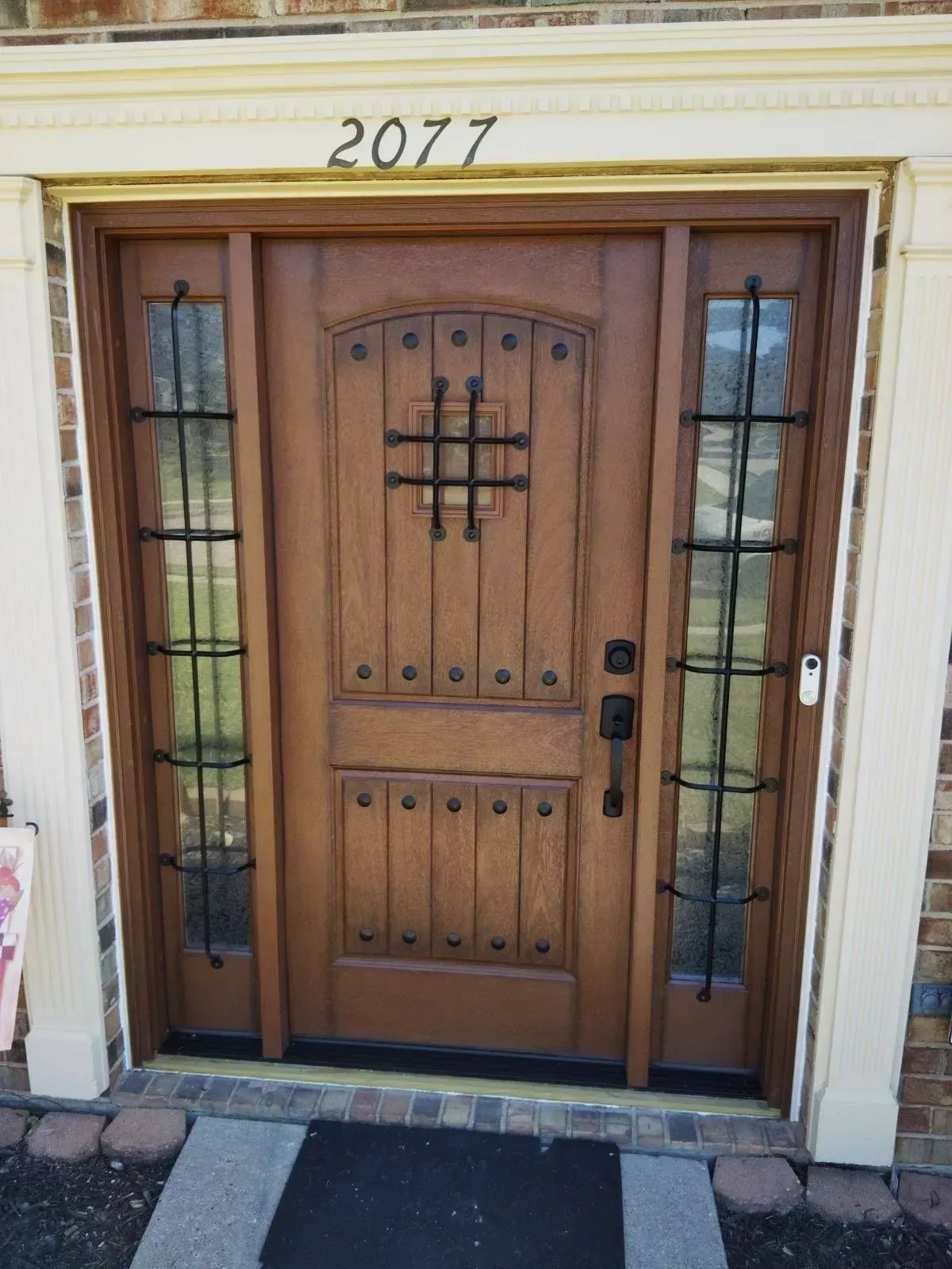 Wooden front door with side windows, iron bars, and the number 2077 above.