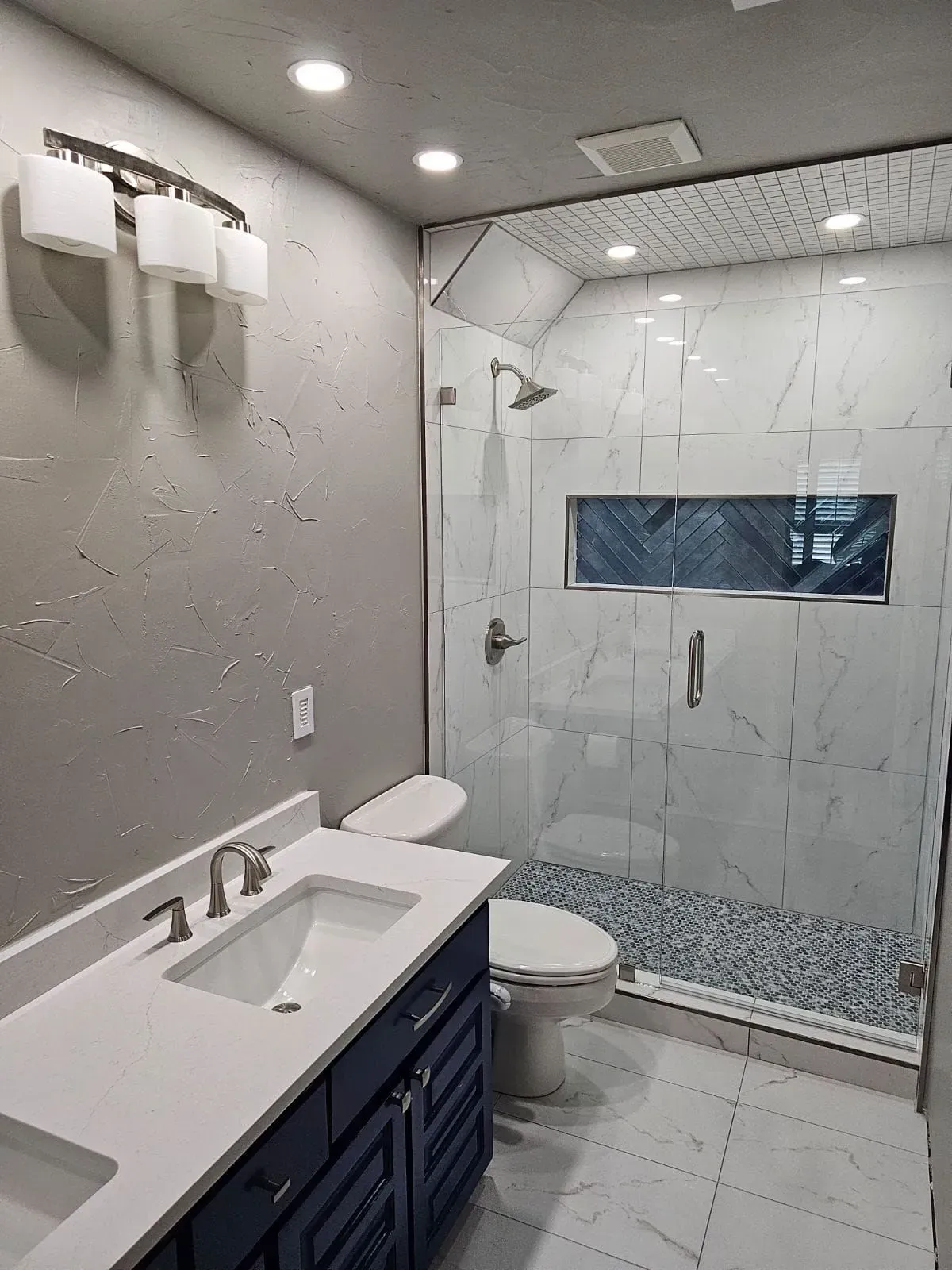 Modern bathroom with blue vanity, white countertop, marble tile shower, and pebbled shower floor.