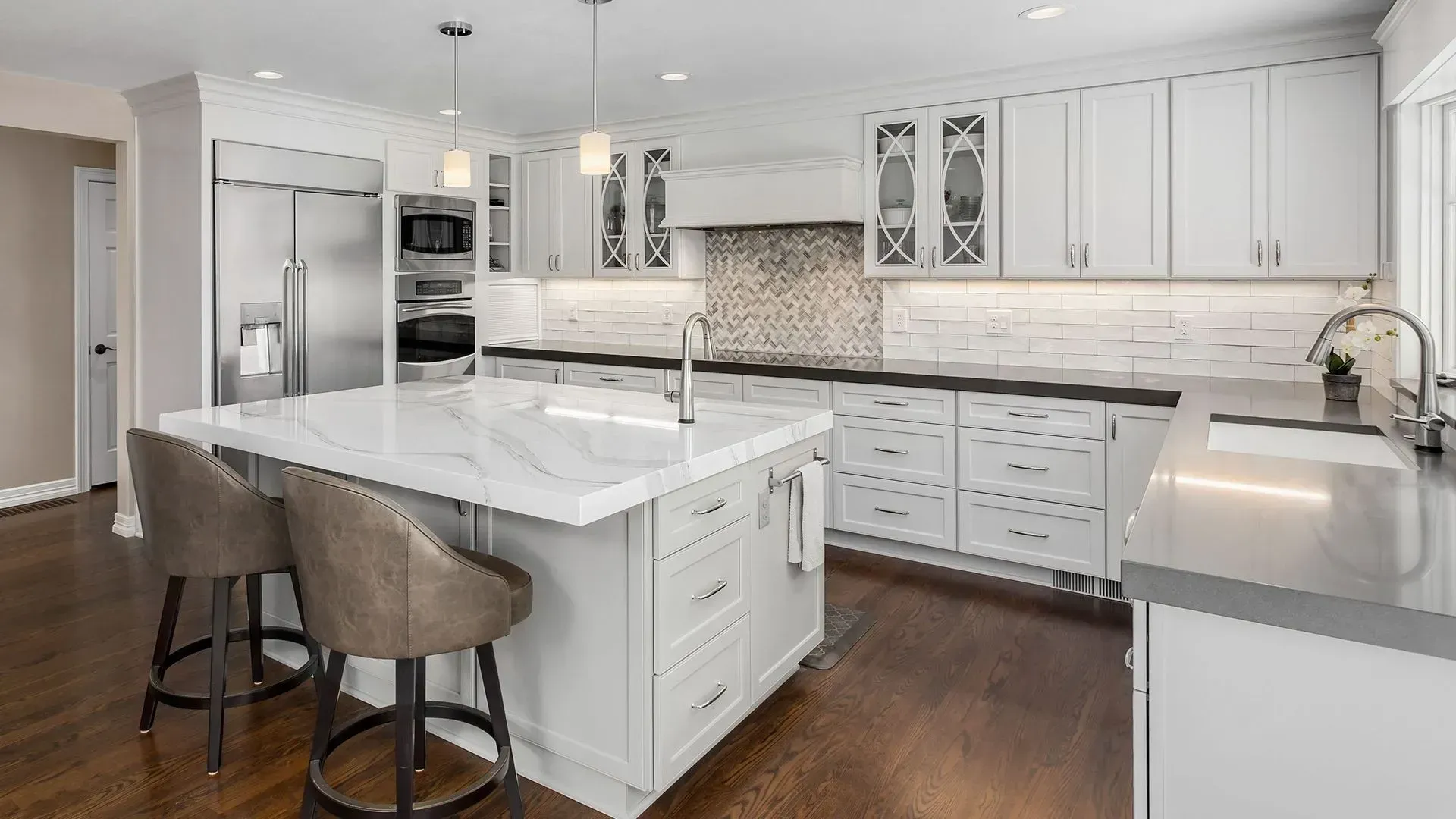 Modern white kitchen with island, marble countertops, stainless steel appliances, and two bar stools.