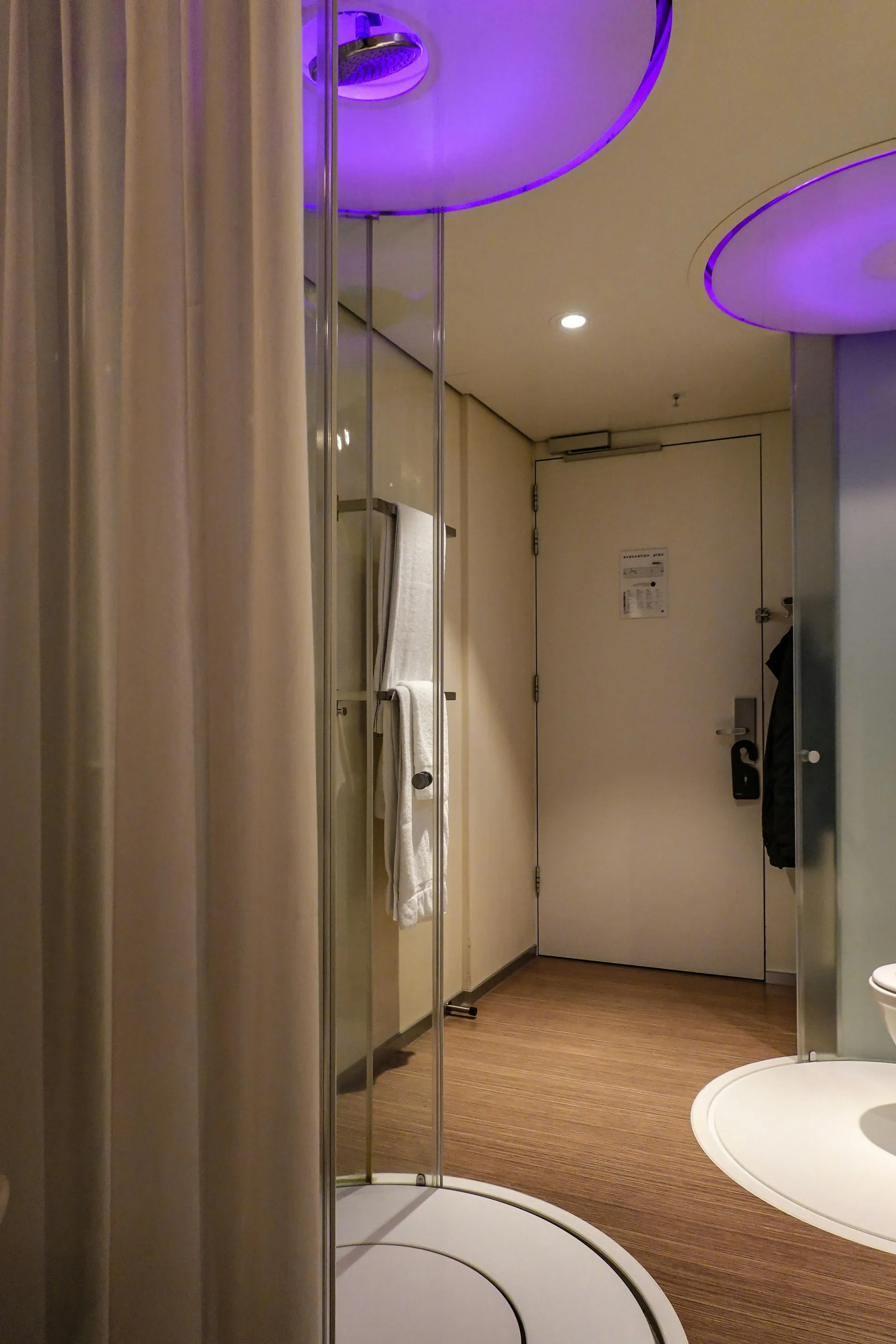 Modern bathroom interior with glass shower, white fixtures, and purple ceiling lights
