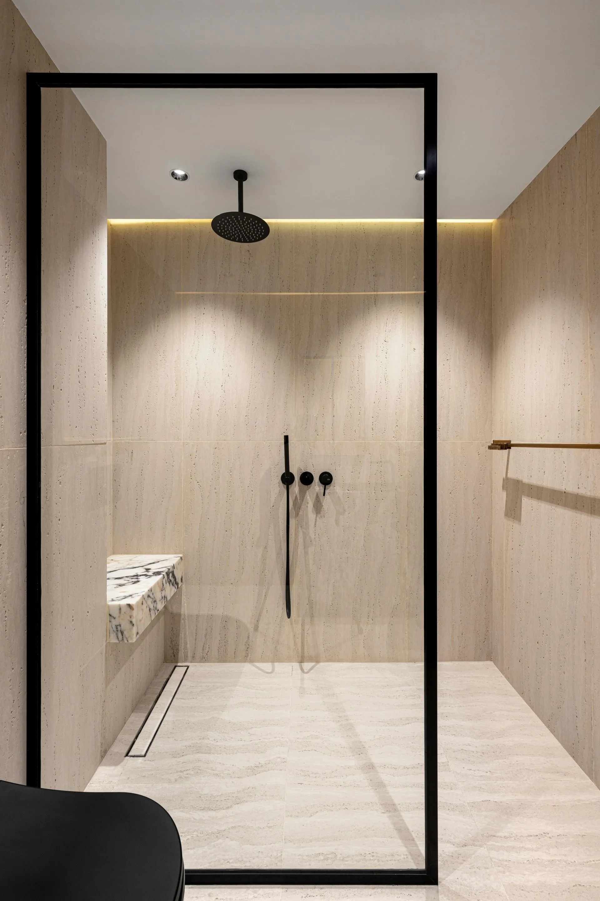 Modern minimalist bathroom with glass shower, beige tile walls, black fixtures, and a marble sink counter
